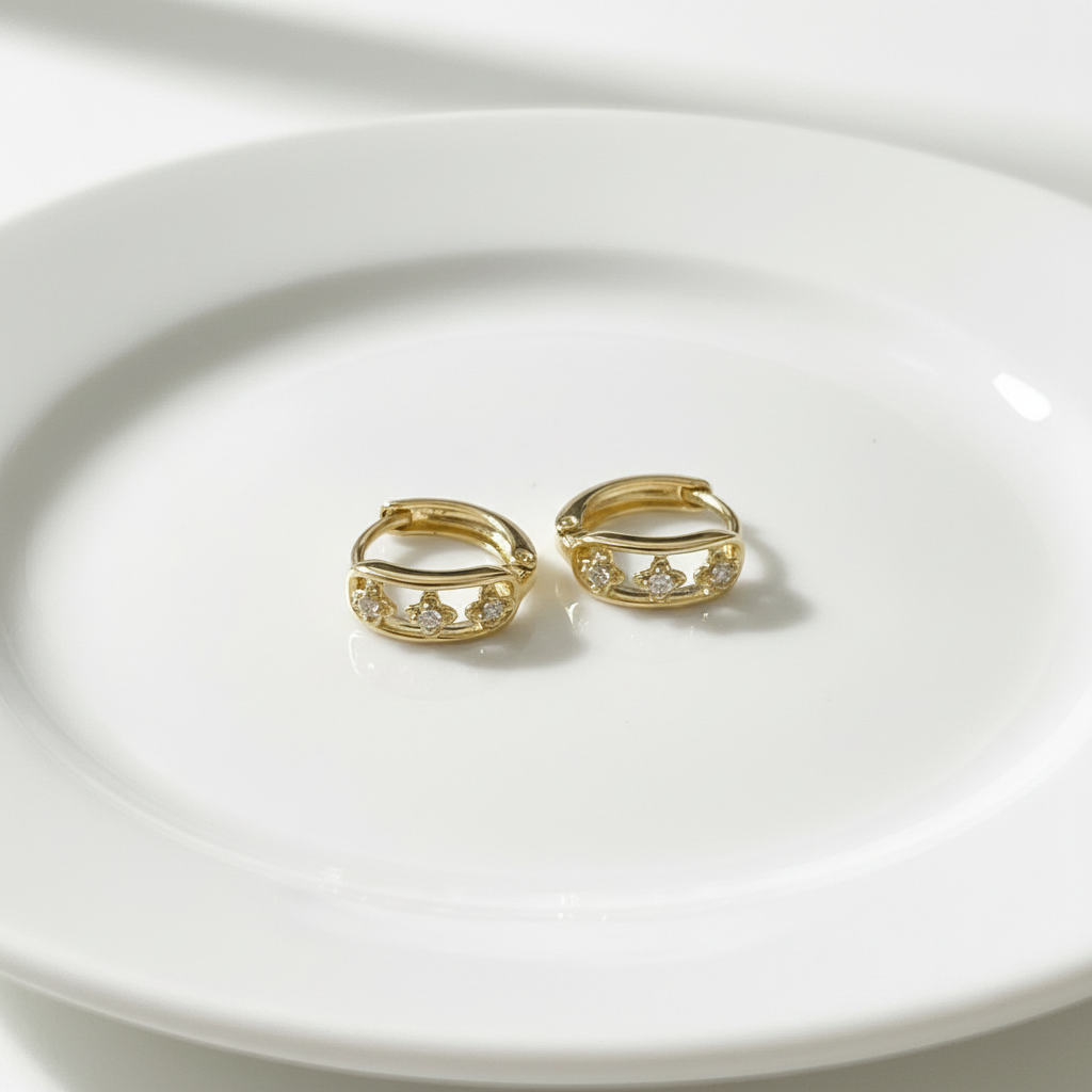 A pair of gold-colored mini hoop earrings with intricate design details.