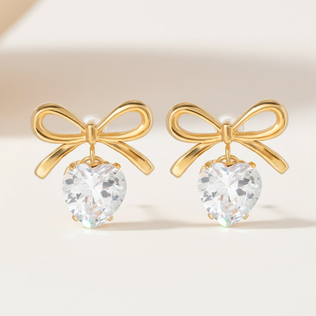 A pair of gold-plated earrings featuring a diamond stimulant heart design with a bow detail.